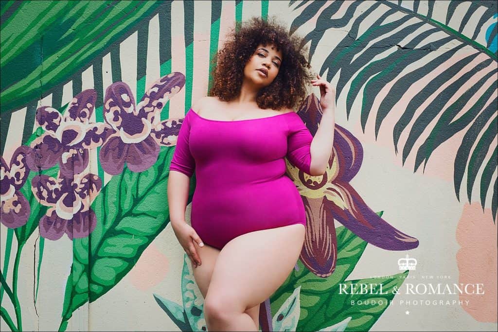 mixed race plus size woman with afro posing in front of a tropical wall mural