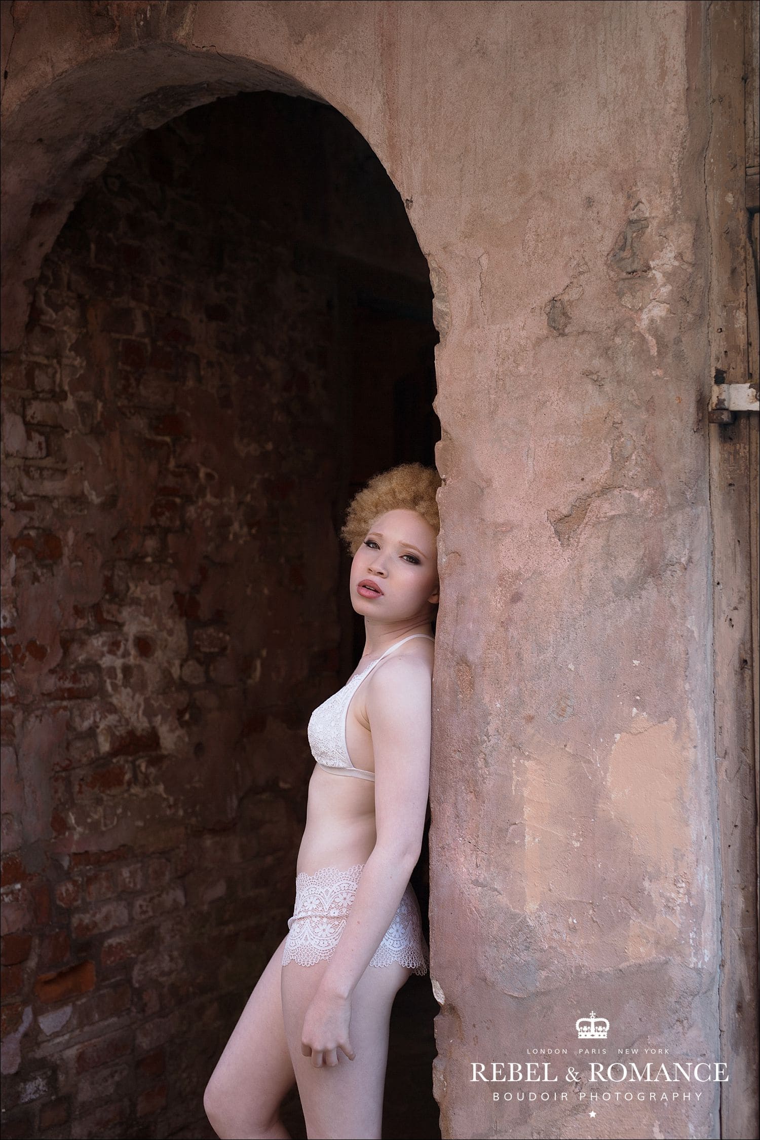 albino woman in white lingerie leaning against old wall