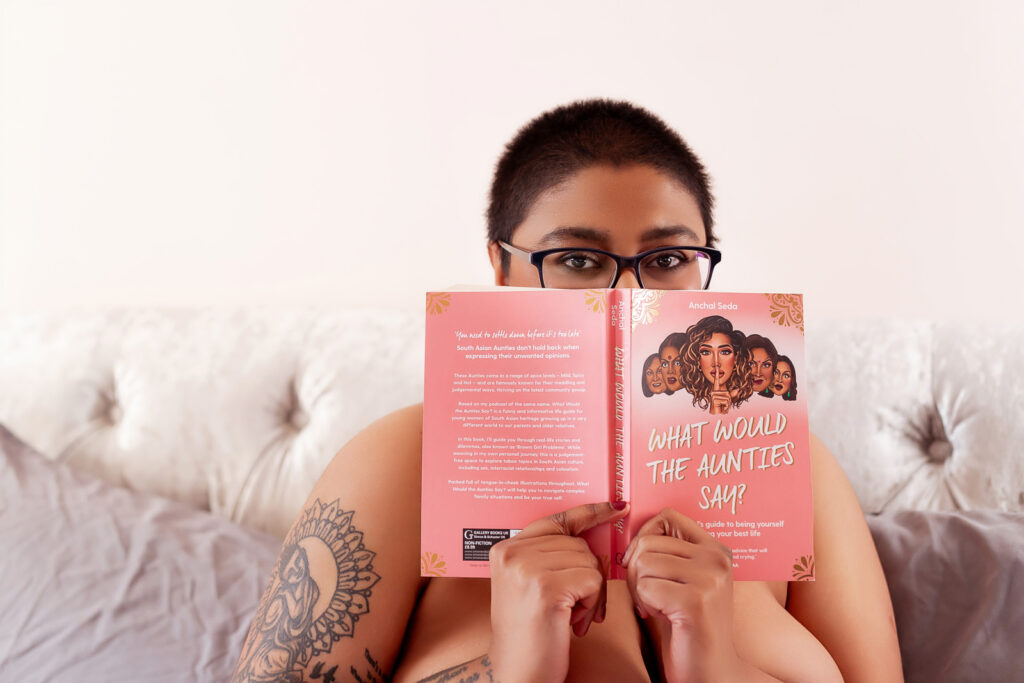 Playful boudoir portrait of a curvy British South Asian woman reading a book in bed during a Suffolk boudoir photography session