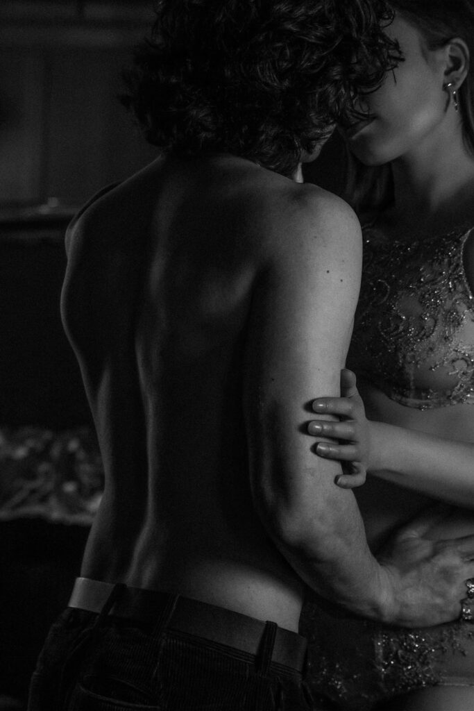Couple in intimate embrace in dark hotel room, romantic London boudoir session