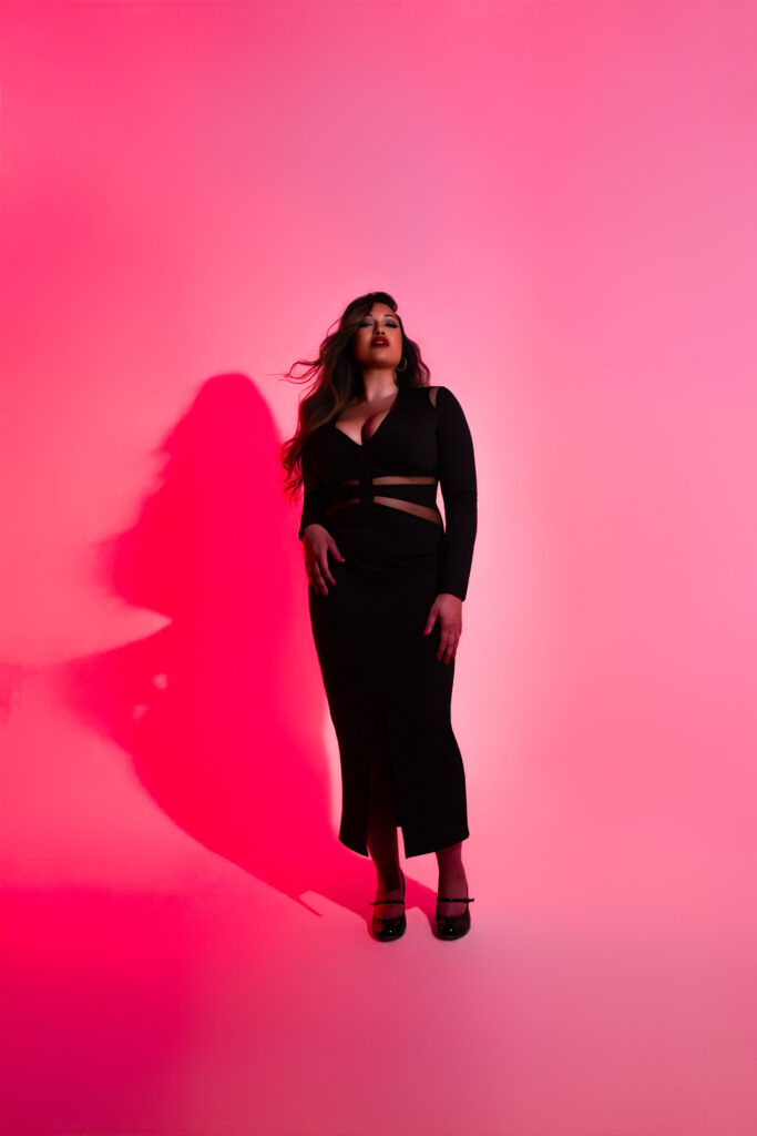 Dramatic editorial image, full length black dress on a curvy woman, in pink studio lighting, black dress