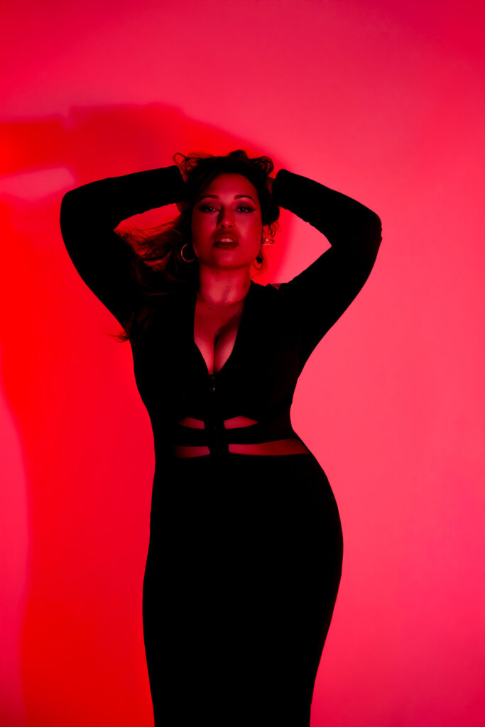 Low lit portrait in pink and red studio lighting, dramatic pose, long black dress