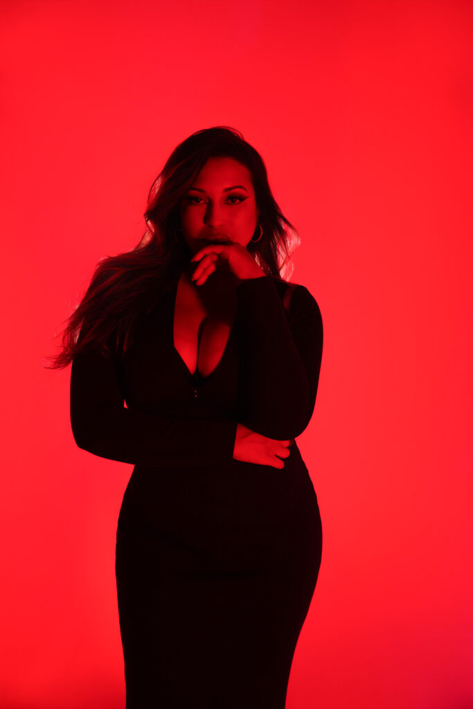 Provocative photoshoot of curvy woman with hand on chin, red lighting and red background