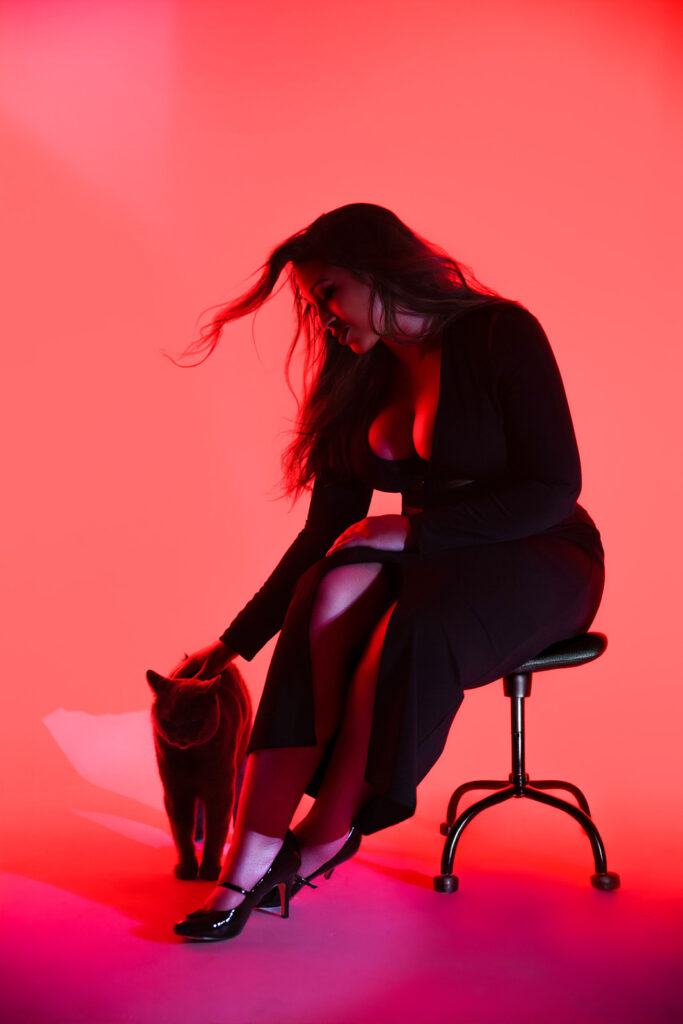 professional photo shoot of a woman in pink lighting, black cat at her feet
