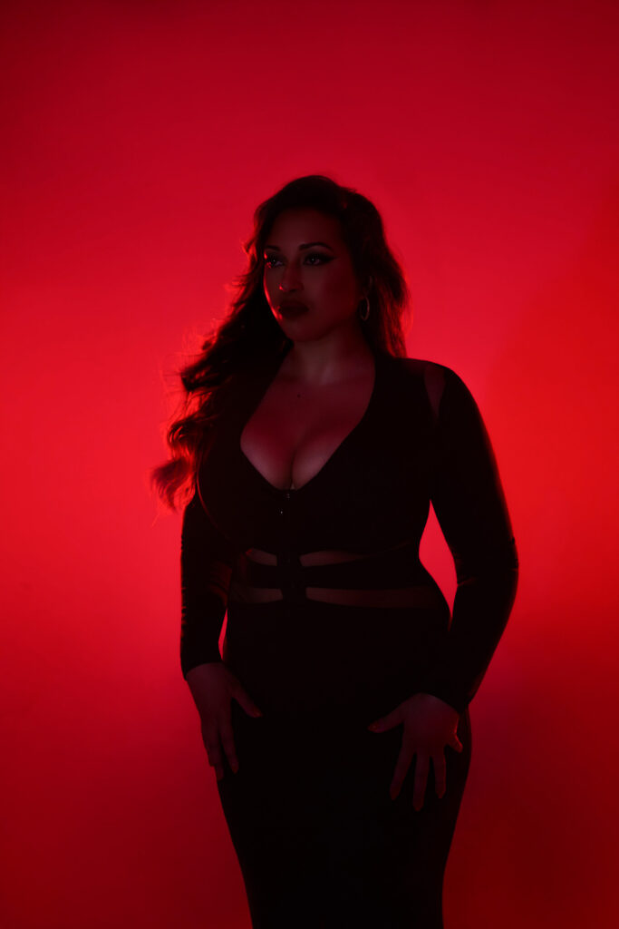 Woman posing in a black dress with hands on hips, red studio lighting