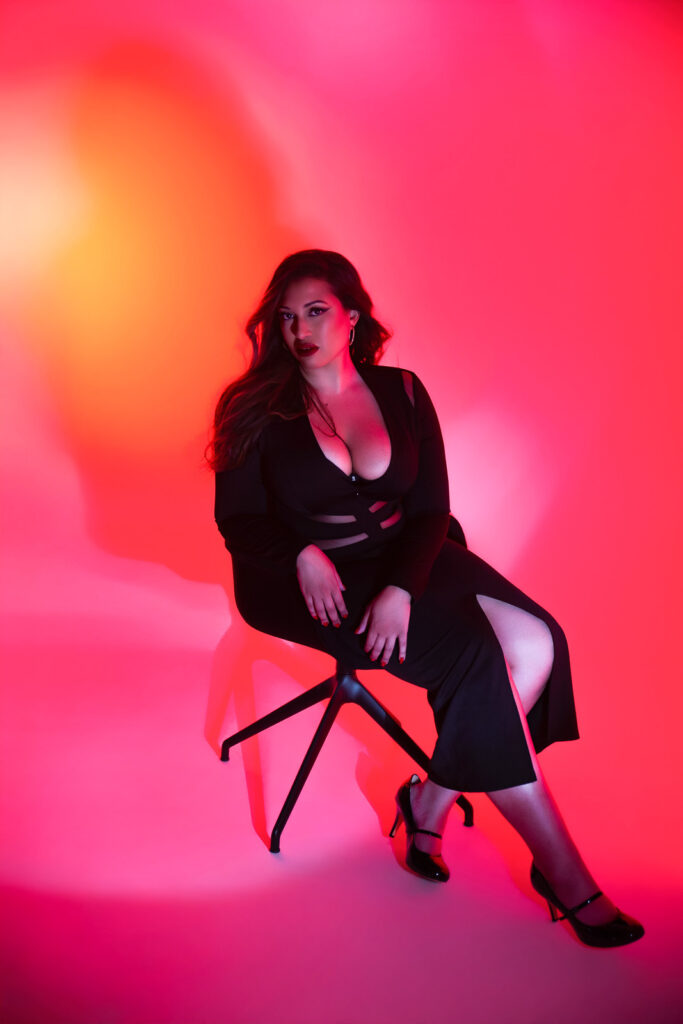 Curvy woman on a chair during a boudoir photo shoot in a cyclorama studio, dramatic red, pink, and yellow lighting