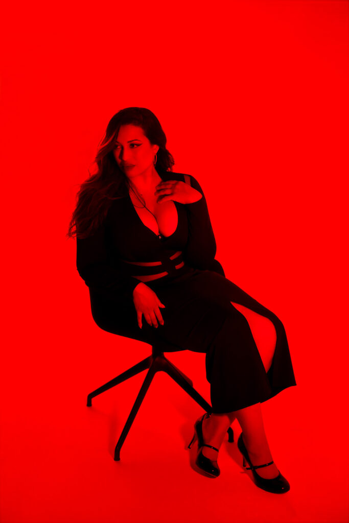 Red on red portrait of a voluptuous woman sitting in a chair, RGB light in a London studio