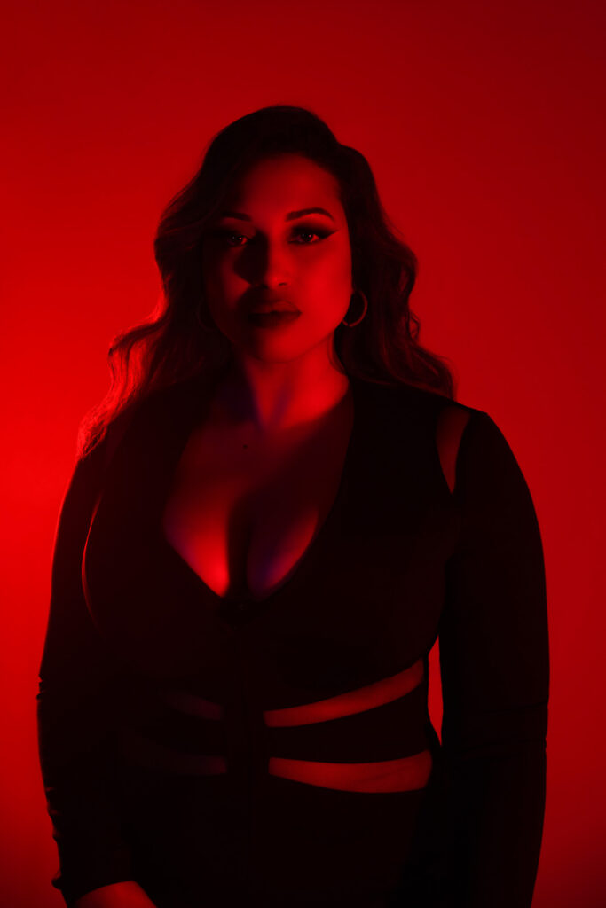Curvy boudoir photoshoot portrait, deep red lighting, black fitted dress