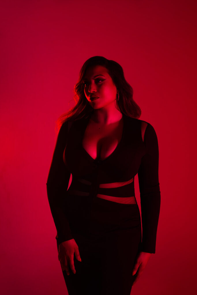 Curvy boudoir photoshoot portrait, deep red lighting, black fitted dress in London