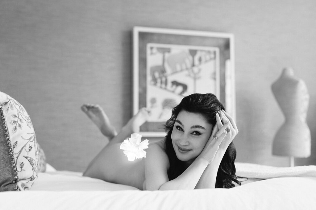 black and white portrait of a smiling woman lying on a bed beside a vintage dress mannequin