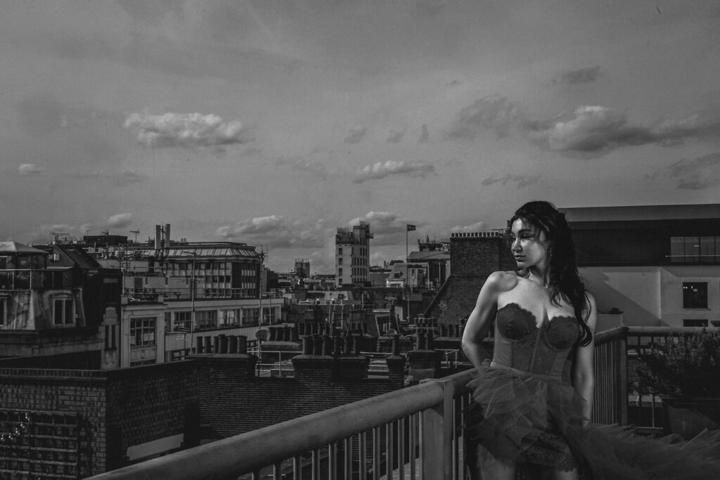 woman standing on a London rooftop terrace at dusk, London skyline in the background