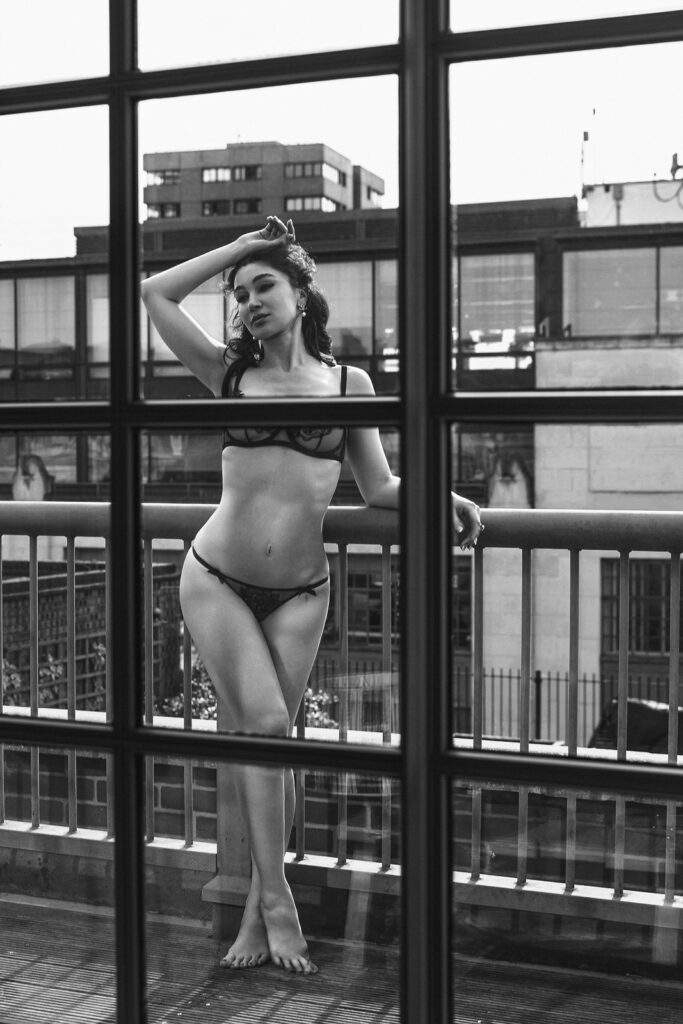 woman in lingerie standing at floor-to-ceiling windows, London high-rise view